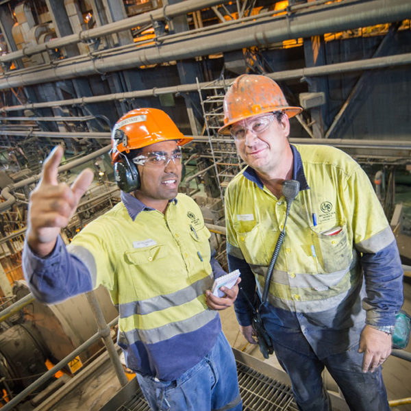 Melwyn Jerome, Safety Advisor, and Todd Allen, Operator (WorkPak) discuss workplace safety at the Zinc Lead Concentrator at Glencore's Mount Isa Mines. The photographer is Rob Parsons of Through The Looking Glass Studio. The image orientation is landscape.